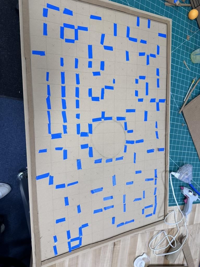 Early cardboard maze grid marked out in blue tape during layout planning